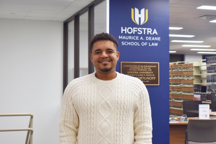 Hofstra Law student Semba Mwitanti standing and smiling in the law library.