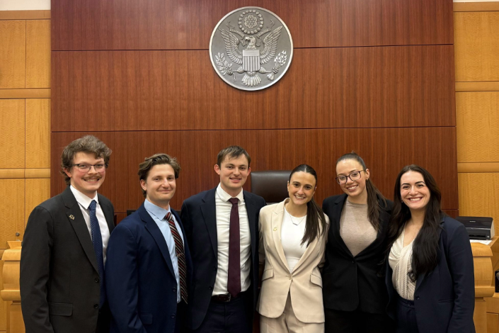 Six law students in business attire standing in a courtroom after moot court competition, National Appellate Advocacy regional semifinalists.