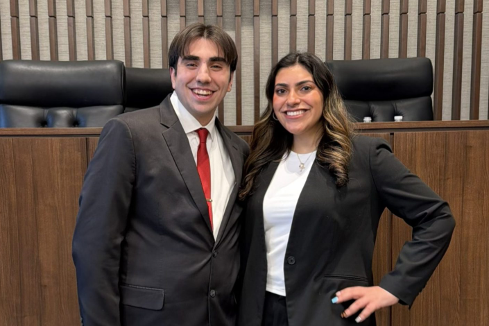 Two students from the Hofstra Law Mock Trial Team smile and pose together for a picture in a court room.