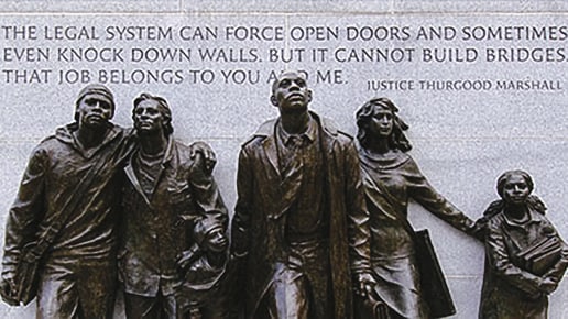 A bronze sculpture of five people stands before a stone wall engraved with a quote by Justice Thurgood Marshall about the legal system’s limits and responsibility, highlighting the need for societal effort to build bridges.