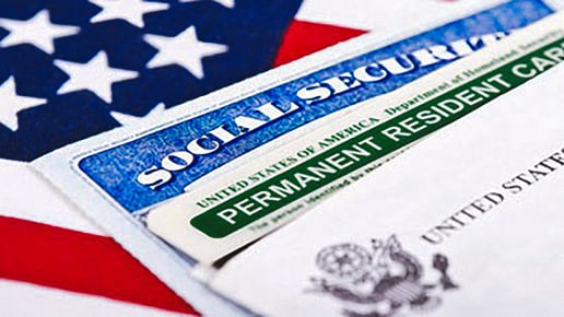 A close-up of a Social Security card and a Permanent Resident Card (Green Card) placed on top of a partial image of the American flag.