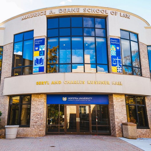 Front entrance of Seryl and Charles Kushner Hall at the Maurice A. Deane School of Law, Hofstra University, with large glass windows, banners, and signage above the main doors.