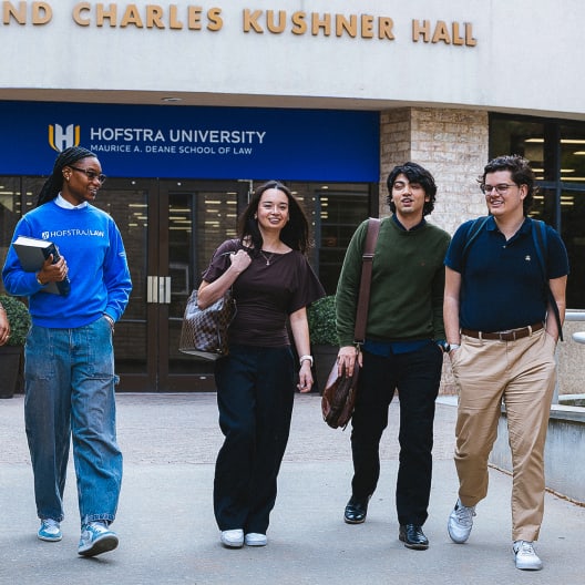 Four students are walking and talking outside the entrance of Hofstra Universitys Maurice A. Deane School of Law, with the building sign visible above them.